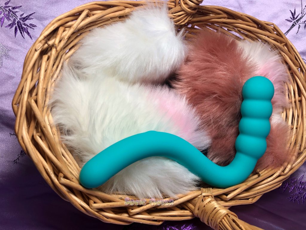Calexotics Pretty Little Wand Bubbly in a wicker basket with fake fur. The wand is an aquamarine blue color.
