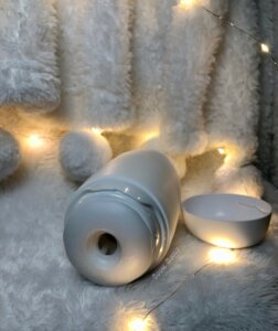 Tenga Puffy Sugar White, a stroker, laying on a fuzzy white material, soft warm lights surround it. 