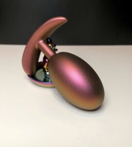 Blush Matrix Neutron butt plug propped against a jewelry holder.