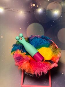 The Maia vibelite maci. A small teal and magenta vibrator. Sitting in a fuzzy, miniature tie-dye.