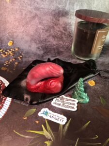 Mr. Peacock packer in merlot and rose sparkle coloration, miniature model squish, and stickers, laying with a black storage bag. The stickers read "no knives, only spoons" and "the early bird has anxiety".