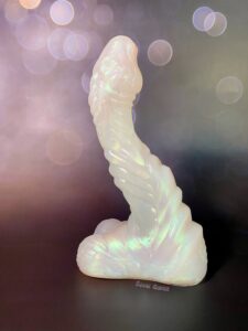 Mothman dildo from Squidly Co. against a black bokeh light background. The silicone dildo is in opal gemstone coloration (sparkly white, white pink and green under stones).