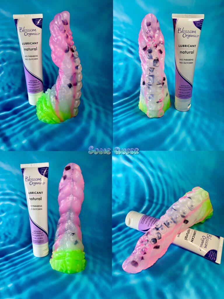 Four picture collage of the Levaina tentacle dildo in "dragonfruit" coloration which is pink and clear, with black "seeds" inside. The base is bright green. The dildo is posed next to a four ounce tube of Blossom Organics lube for size comparison