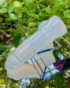 Elwyn dildo posed laying on top of the mirror, the ball base end is propped up and the head is downward.