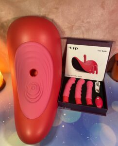 The VVD Rider Desire, a sex saddle, propped up with the box of three included attachments beside it. The User Manual, remote control, and charging cable in the box, too.