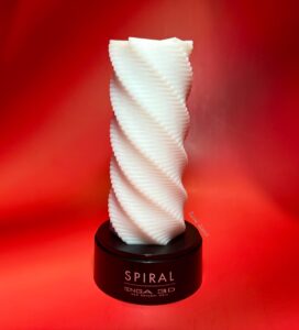 Tenga 3D Spiral on its black stand against a red background. A white, T.P.E stroker. The stand says Spiral Tenga 3D New Concept Hole. 