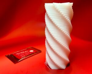 Tenga Spiral 3D standing up on its own, the satchet of lube lays in the background. 