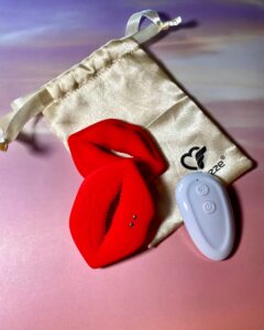 One lip nipple clamp is displayed with the front showing, and one lip nipple clamp is displayed with the back showing. The white remote control can be seen, as well/ 