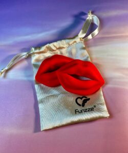A pair of red silicone lips. They're lip shaped vibrating nipple clamps, laying on top of a silky, gold-colored drawstring pouch. 