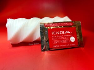 Spiral 3D laying on its side with a satchet of tenga hole lotion lubricant propped against it. 