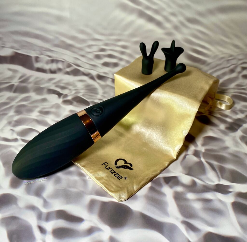 Funzze Orgasm Monster Pro laying on top of a box covered by the gold storage bag. Both silicone attachments are sitting next to it.