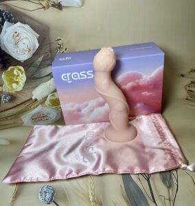 Rose bendable dildo, in pink color, from Crassie propped against the Crassie box with a pink silky drawstring storage bag. 